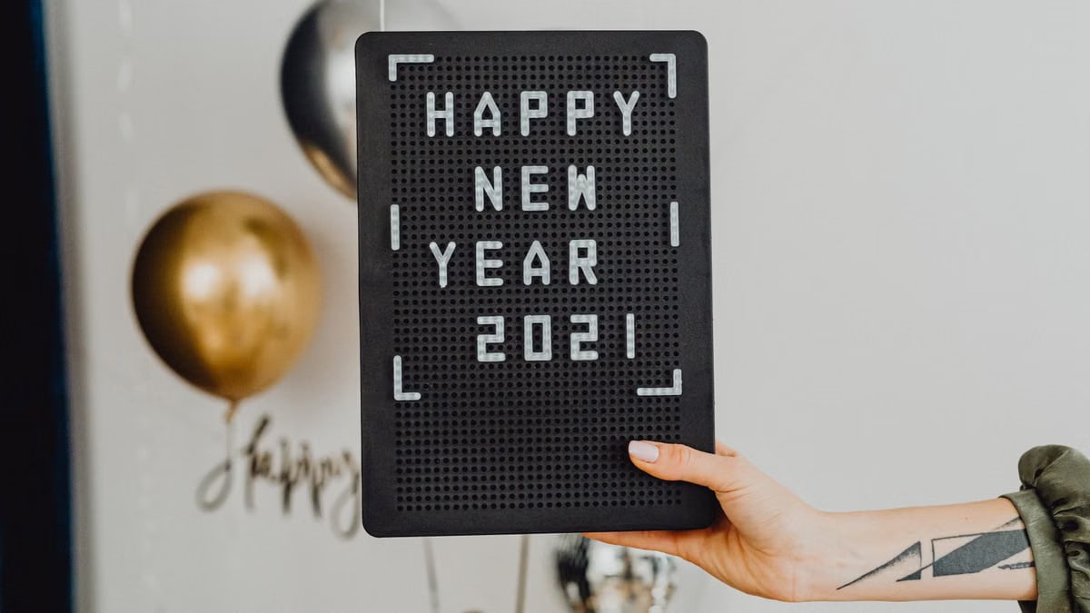 Hand holding a letter board with 'Happy New Year 2021' message, adorned by balloons in the background.